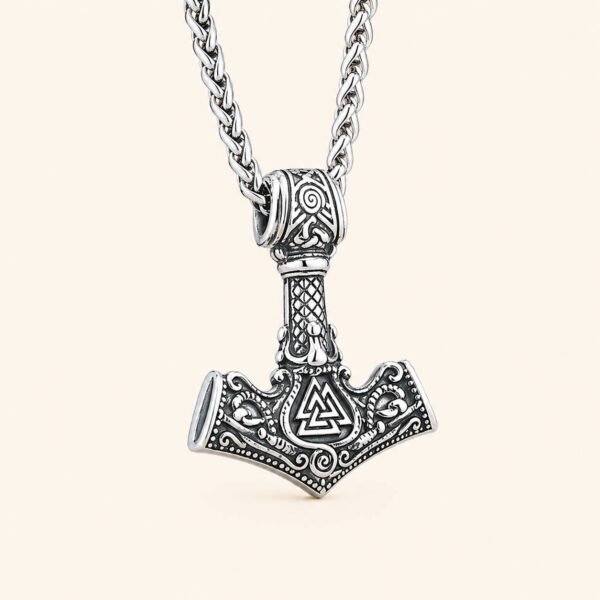 detalle-colgante-mjolnir-vikingo-valknut-acero-316l Colgante Mjolnir de Thor con Valknut en acero inoxidable 316L sobre fondo claro minimalista